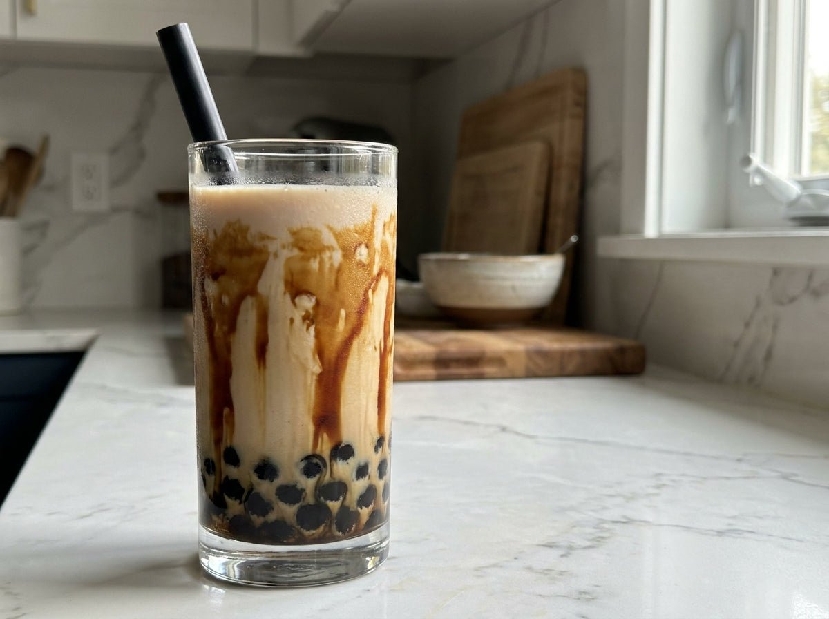 Tall clear glass of homemade ube boba with creamy lavender milk, dark brown sugar tiger stripes along the glass, black tapioca pearls clustered at the bottom, wide black boba straw