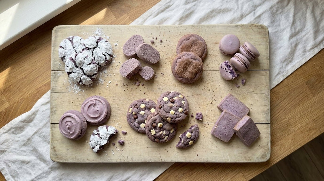 Overhead spread of 7 different ube cookies on a wooden board: crinkles, polvoron, snickerdoodles, macarons, sugar cookies, chocolate chip cookies, and shortbread