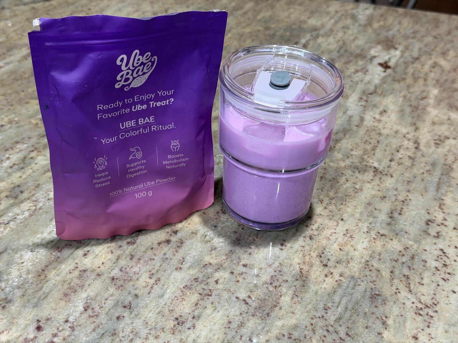 Vibrant purple ube smoothie in a portable blender cup next to a Ube Bae powder pouch on a kitchen counter